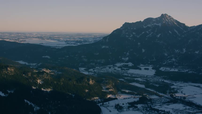 Dusk is settling over a snow-covered mountain range and valley