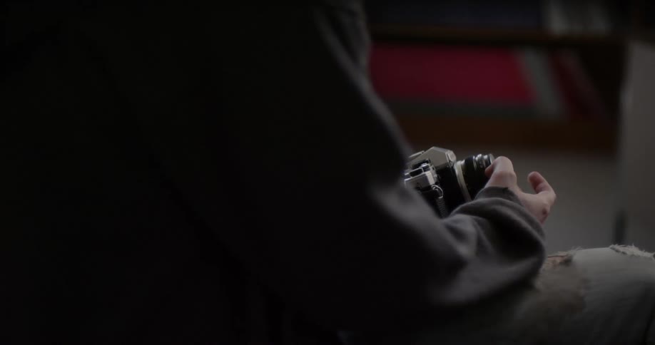 A man is fidgeting with the lens cap on his camera as he sits