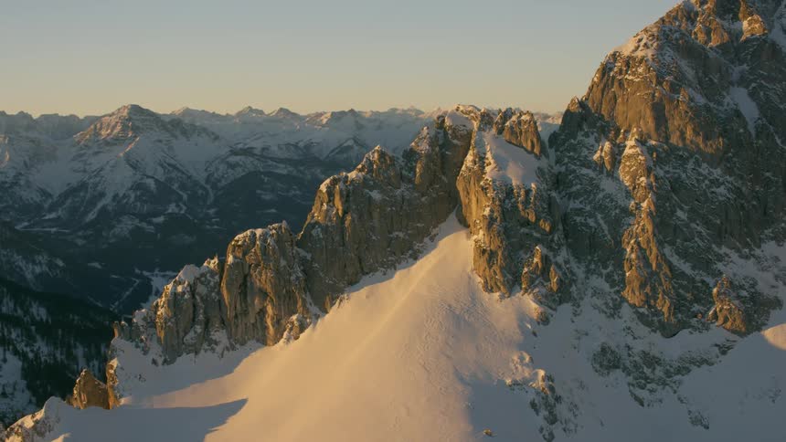 Snow blankets the slopes of a mountain range and valley at dawn