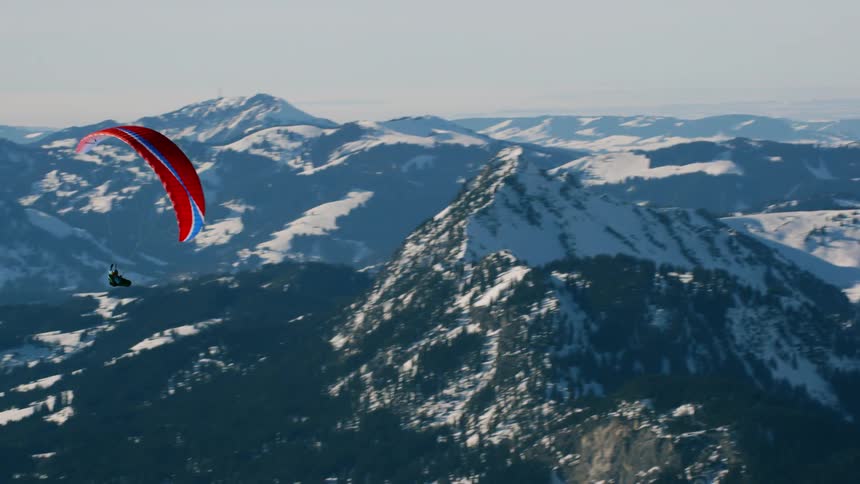 Parachuter floats near a snowy mountain peak