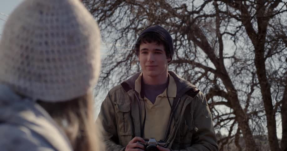 A teenage boy takes a photo of a girl outside on a cold day