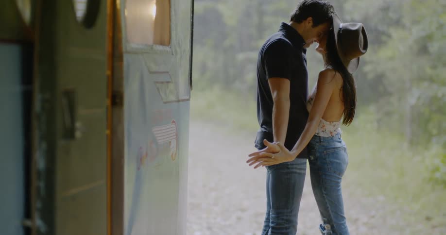 A man and woman are holding hands and kissing the girl is wearing a cowboy hat