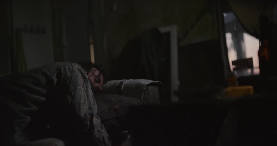 A man sleeps on a couch as a man walks by