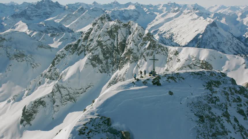 People are gathered around a cross on top of a snow covered mountain during the day