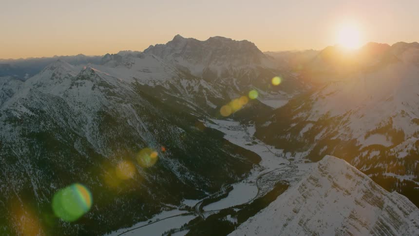 The sun is rising over a mountain range and valley covered in snow