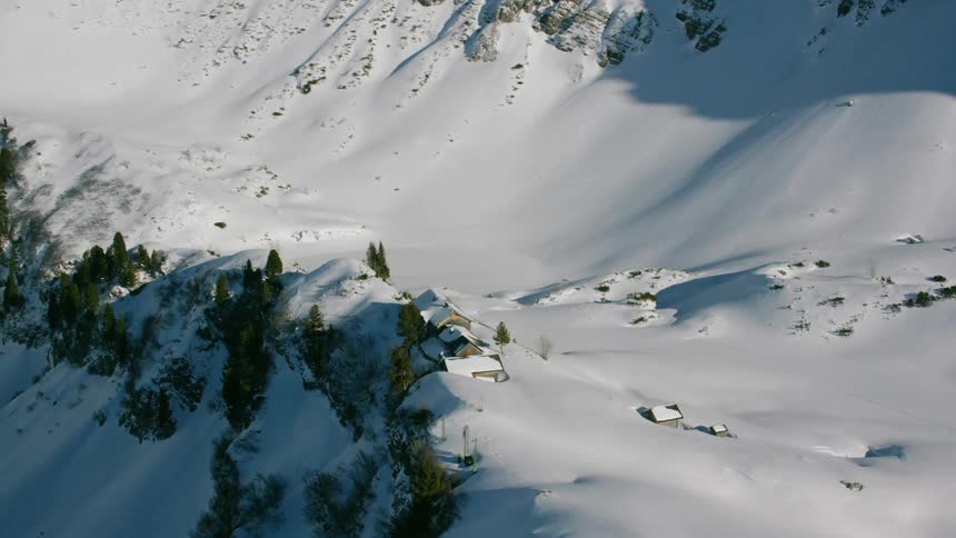 A cabin covered in snow sits on a mountain ridge during the day