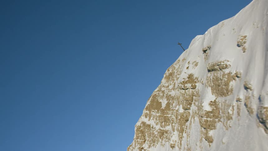 A cross sits atop a snowy mountain
