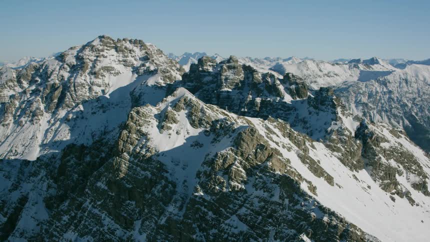 Snow blankets the slopes of a mountain range on a sunny day