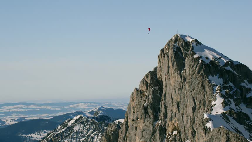 A paraglider is sailing over a mountain peak on a sunny day