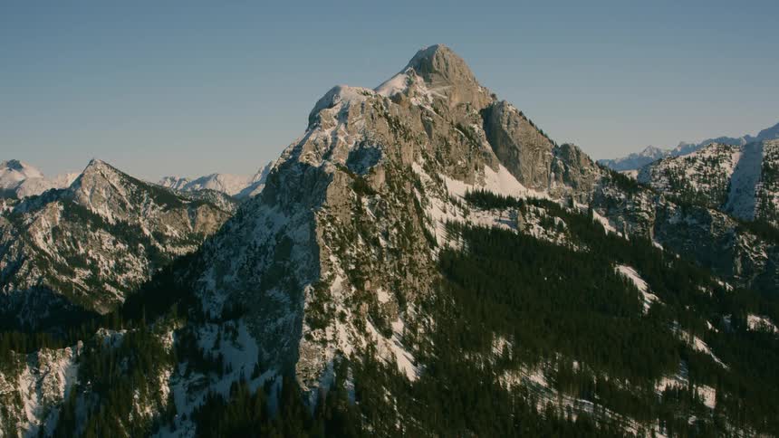 Large mountain range partially covered in snow and trees on sunny day