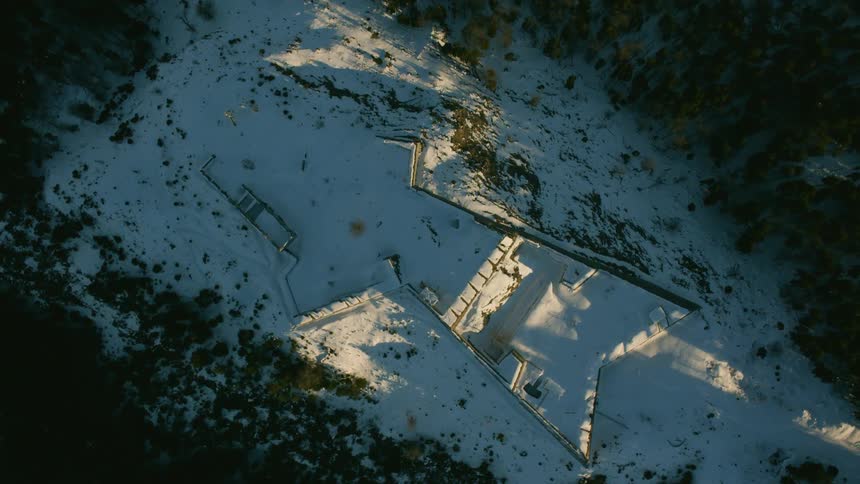 The remains of a large building is nestled in the middle of a forest