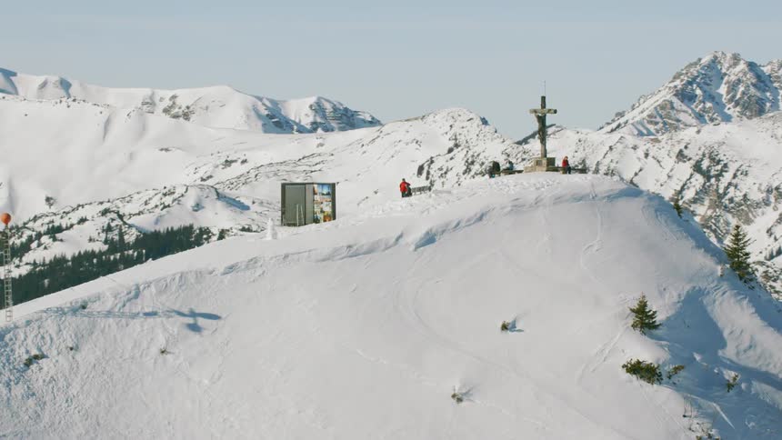 People stand atop a snowy mountain with a large cross
