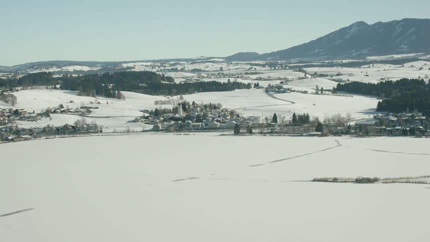 A village sits on the shore of a frozen lake on a sunny day