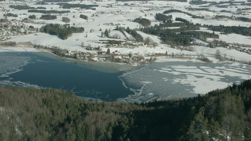 A melting river runs past a village in a winter landscape