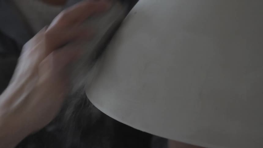 A hand sanding a piece of pottery