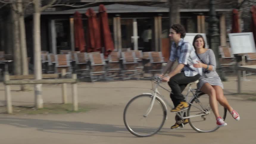 A woman rides on the back of a bicycle as a man steers it