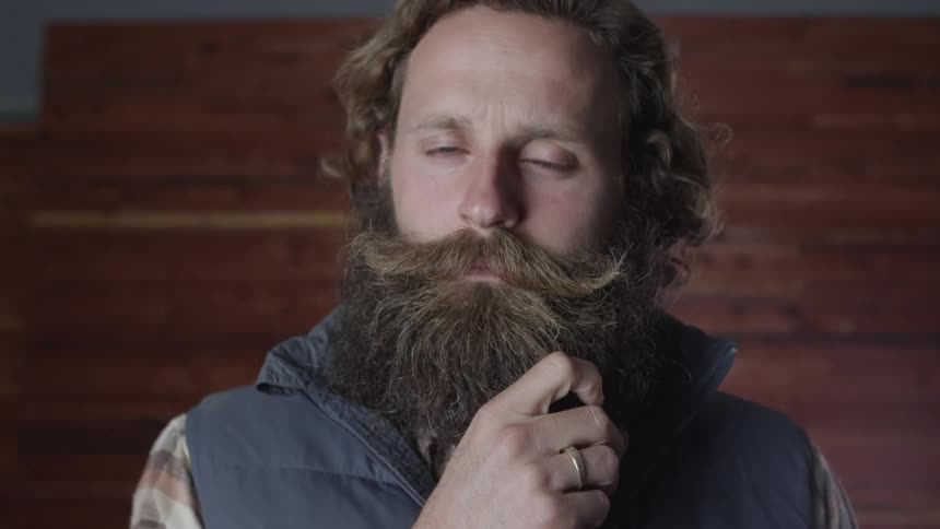 Bearded man wearing wedding band strokes his beard