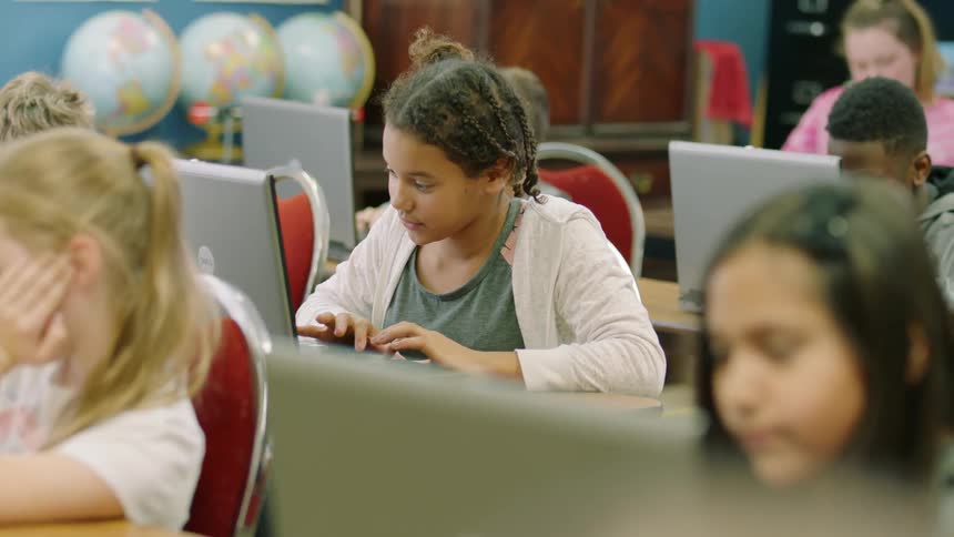 School children sit at desks working on laptops