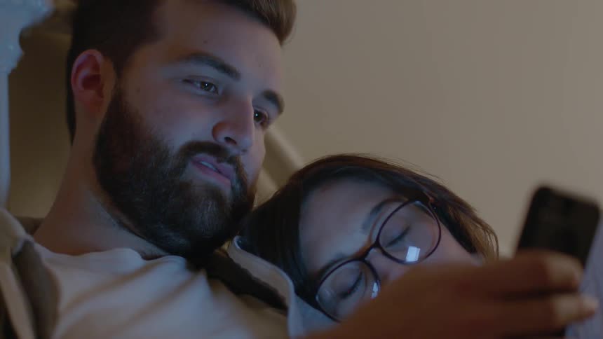 Man and woman look at phone in bed