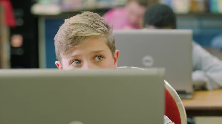 School children sit at desks working on laptops