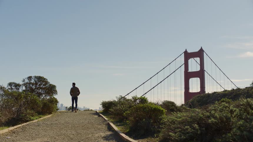 Man walking on path with view of golden gate bridge on sunny day