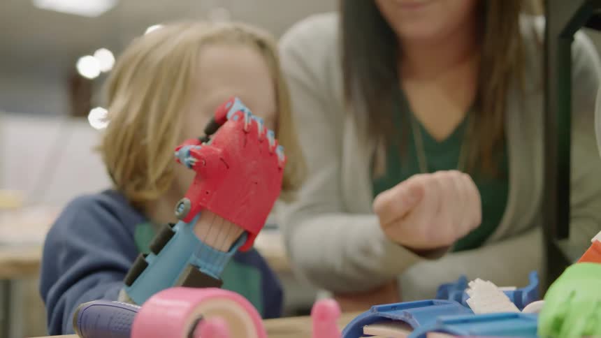 A woman teaches a young boy to use a robotic hand