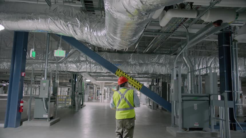 Someone in a safety vest and hard hat is walking through a factory