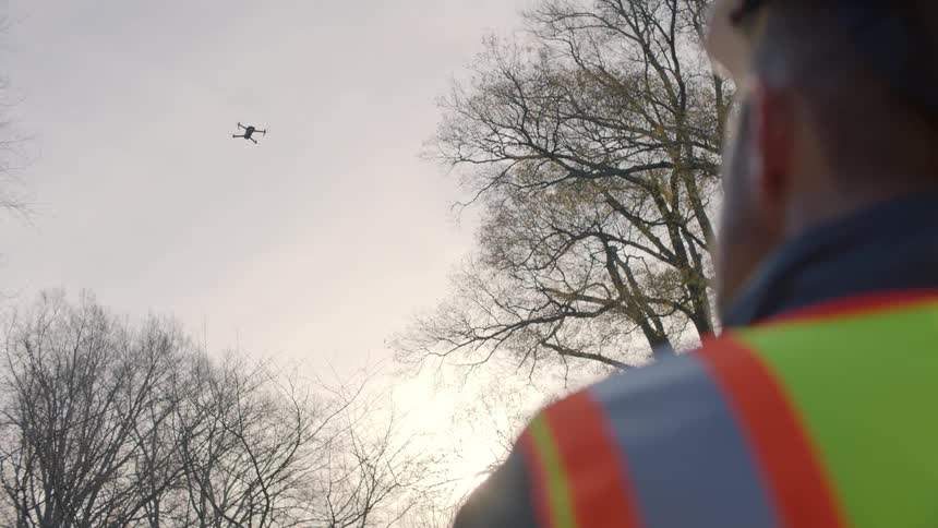 Man wearing a bright yellow vest flies a drone