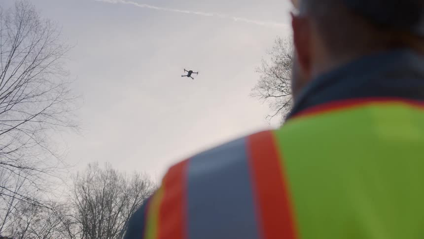 Construction worker watches drone flying in sky