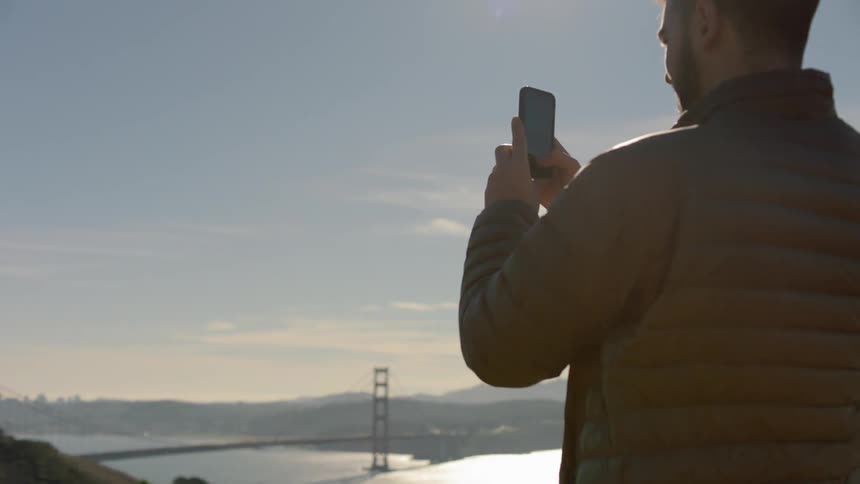 A man is using his phone to take a picture of the bridge