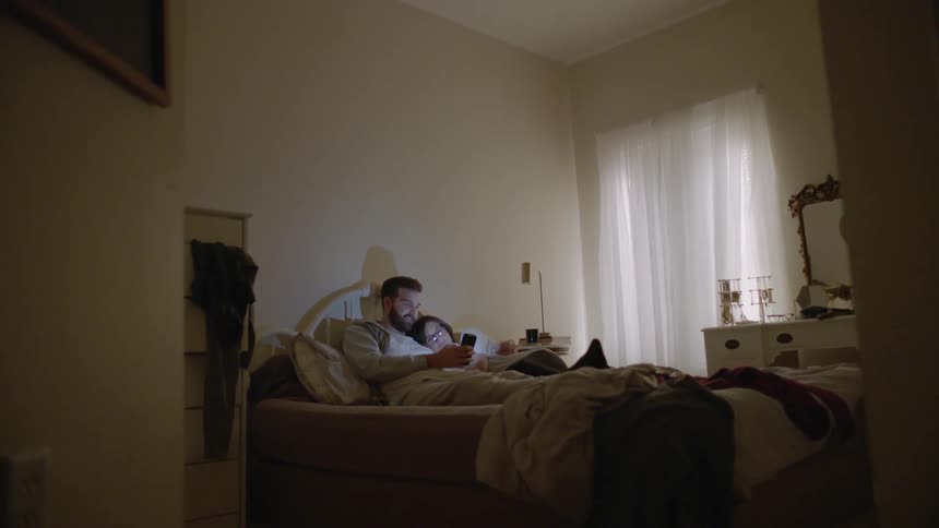Man and woman laying in bed looking at cell phone