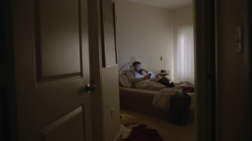 A man and woman lay in bed looking at a phone