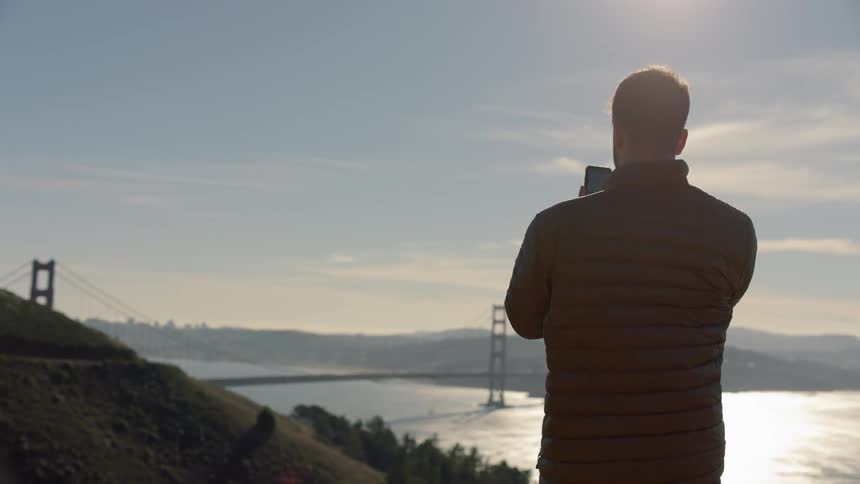 A man is using a cellphone to film the golden gate bridge at dawn