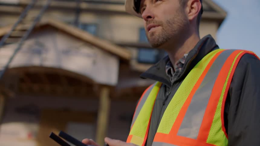 A worker in a hard hat and vest uses a remote to control equipment