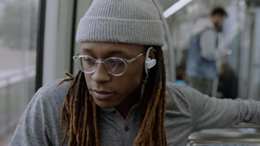 A man wearing earbuds sits on the bus