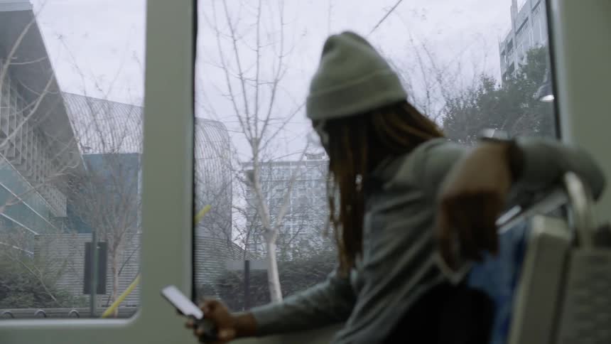 Man types on phone while riding bus as the city passes by