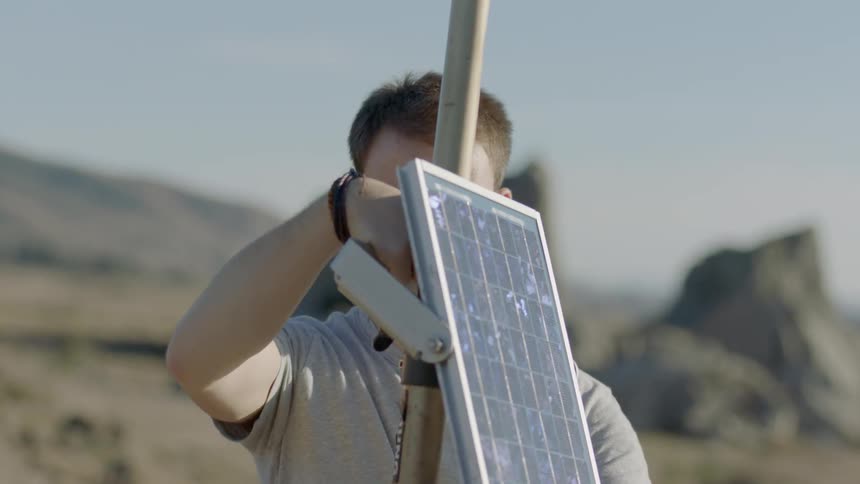 A man is outside setting up a solar panel by the beach
