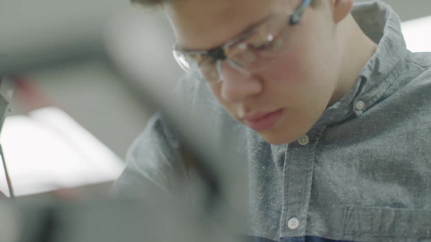 A young man wearing safety goggles works on an object