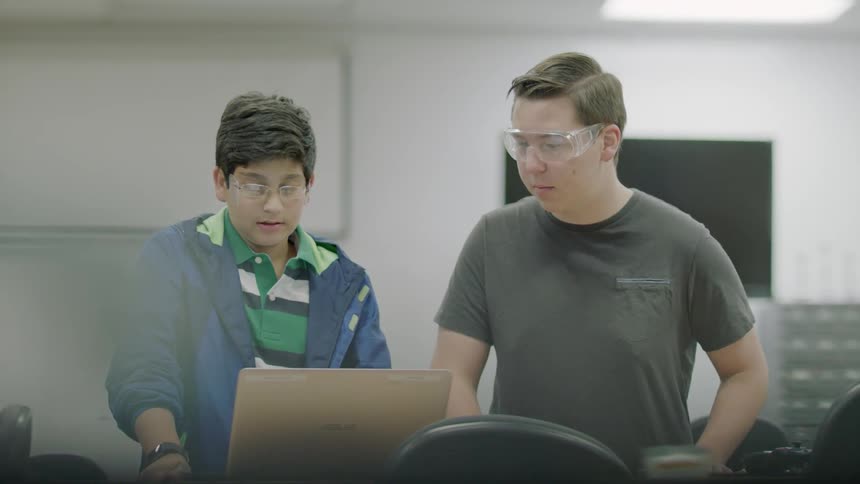 Students wear safety goggles while looking at a laptop