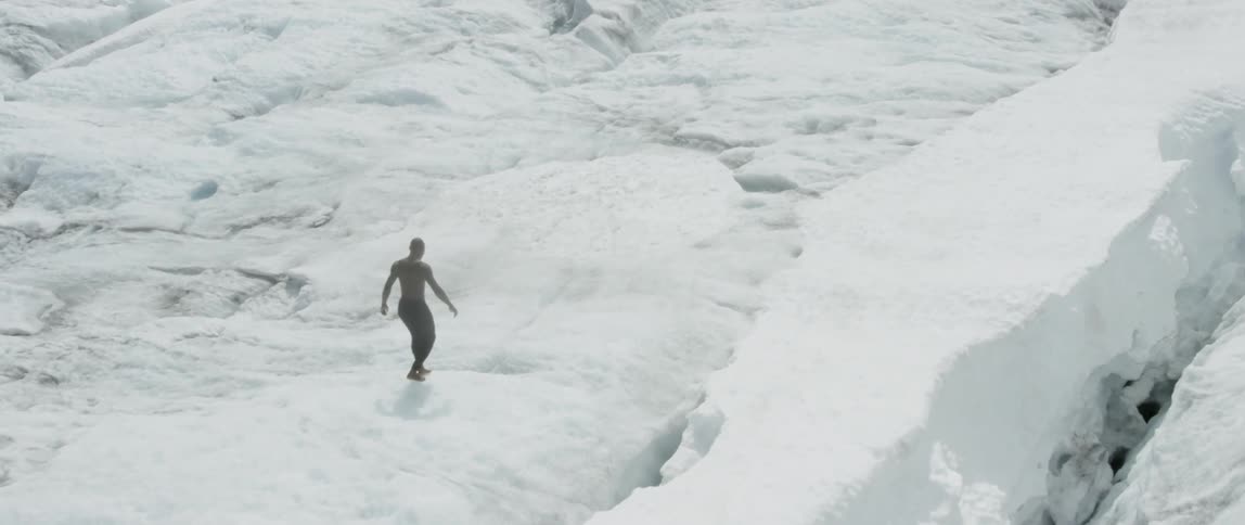 A man is walking barefoot on a glacier during the day