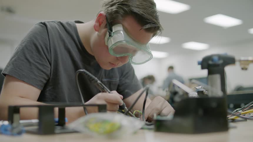 A young man works on electronics with a soldering iron