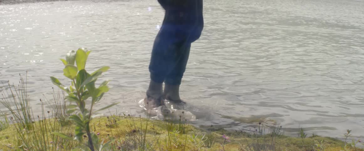 A man wades into a lake and back out on a windy day