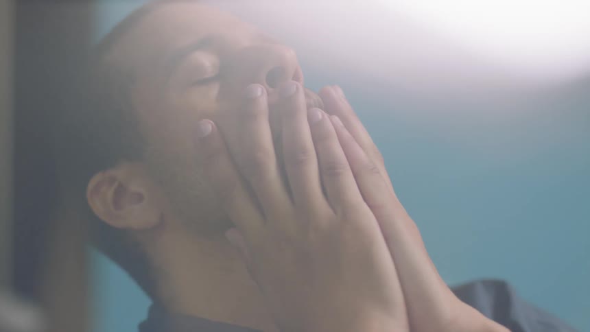 A man wipes his face then looks down shaking his head