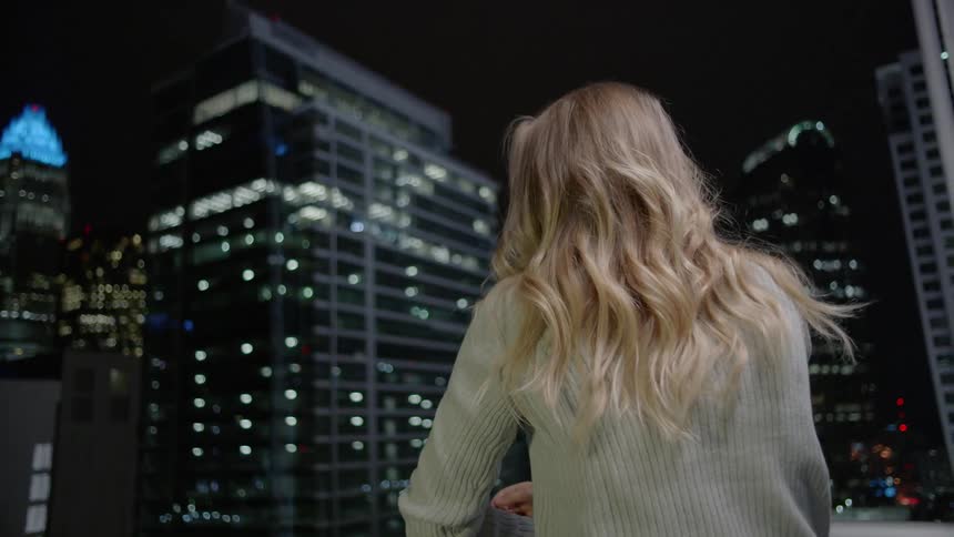 A woman is leaning on a balcony taking in a city view at night