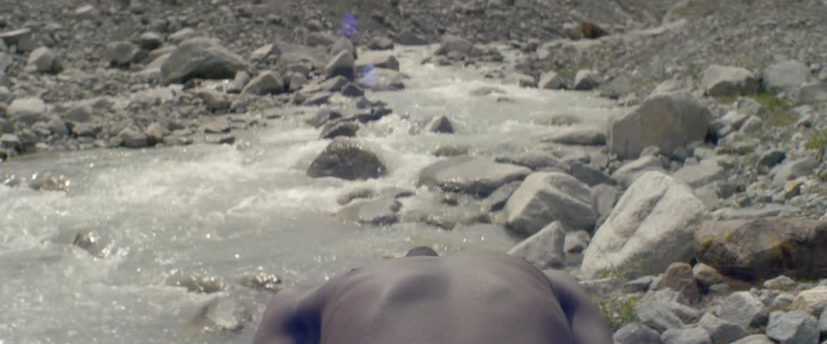 Man lays outside on rocks next to a stream