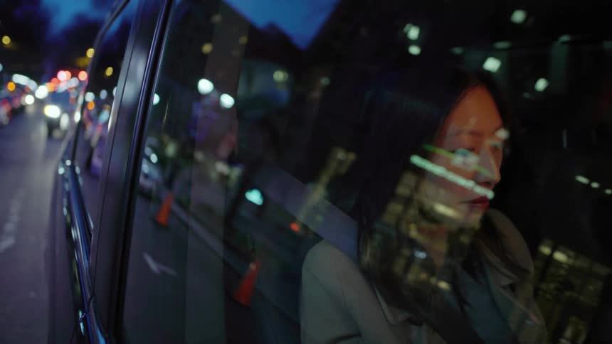 A woman is sitting in a car looking out the window at the city lights