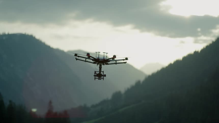 A drone is rising in the sky and flying in a mountain setting on a cloudy day