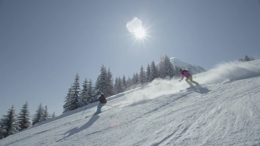 People skiing down a mountain ski slope on a sunny day