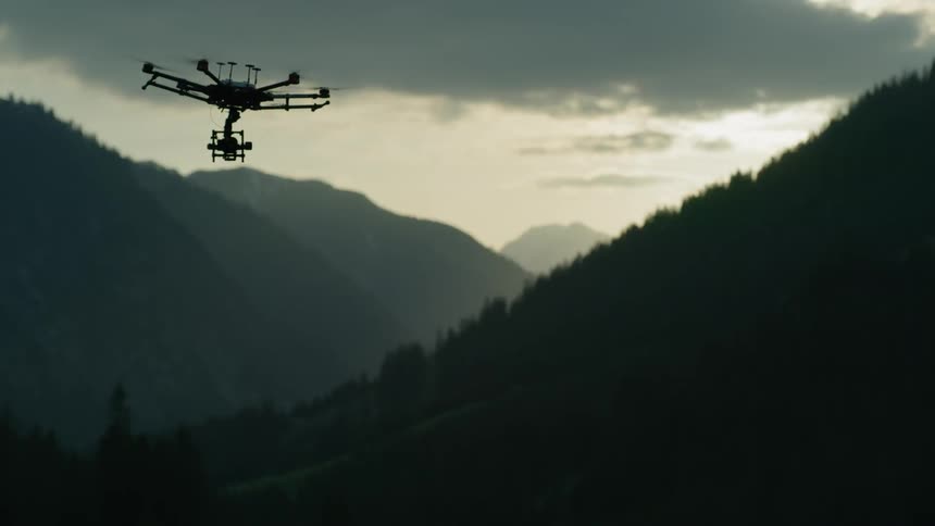A drone is flying over a forest covered hill