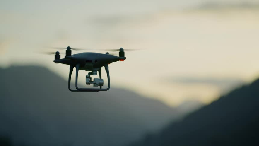 A drone hovers in the mountains at sunset